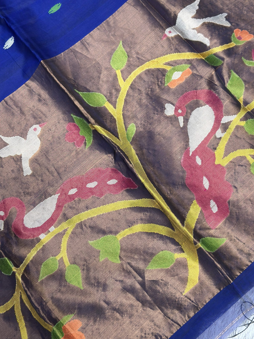 Close-up of woven peacock and flowering vine on royal blue Jamdani